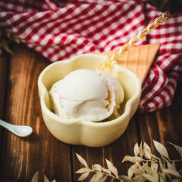 Delightful serving bowl filled with sour cream ice cream that looks like an ice cream cone with ice cream scoops. Placed on a brown wooden background.