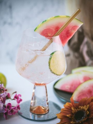 Beautiful balloon like glass filled with refreshing watermelon gin and tonic. Garnished with a reusable drinking straw, a big watermelon slice, and a lime slice.