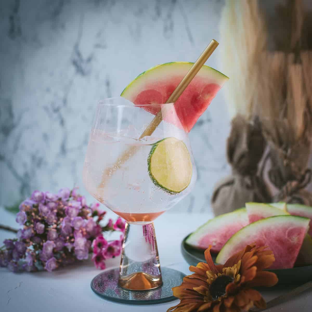 Beautiful balloon like glass filled with refreshing watermelon gin and tonic. Garnished with a reusable drinking straw, a big watermelon slice, and a lime slice.