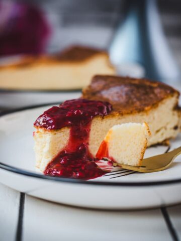 Delicious slice of semolina cheesecake with raspberry topping. Served on black and white plate.