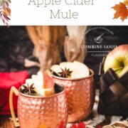 Copper mug, filled with delicious apple cider Moscow mule, garnished with fresh apple slices and a star anise. Placed on wooden board, next to a red cloth.