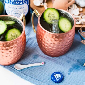 Refreshing mint cucumber Moscow mule served in copper mugs, placed on white and blue ground.