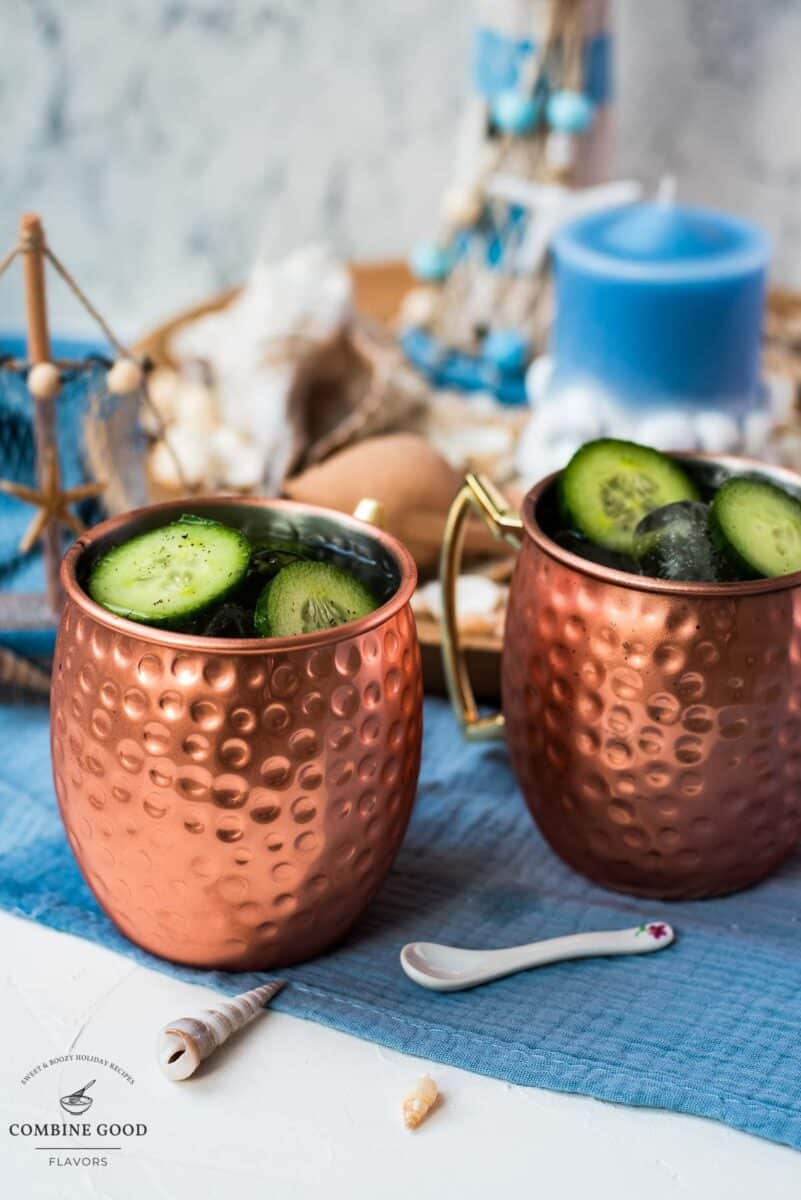 Refreshing mint cucumber Moscow mule served in copper mugs, placed on white and blue ground.