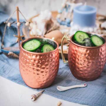 Refreshing mint cucumber Moscow mule served in copper mugs, placed on white and blue ground.