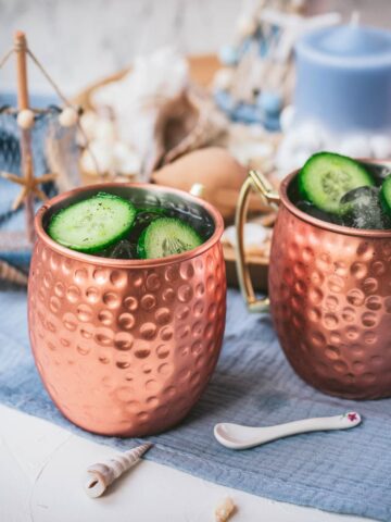 Refreshing mint cucumber Moscow mule served in copper mugs, placed on white and blue ground.