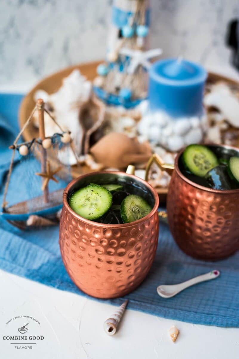 Refreshing mint cucumber Moscow mule served in copper mugs, placed on white and blue ground.