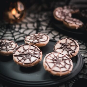 Hauntingly delicious spiderweb cookies, placed on black plate on spiderweb ground.