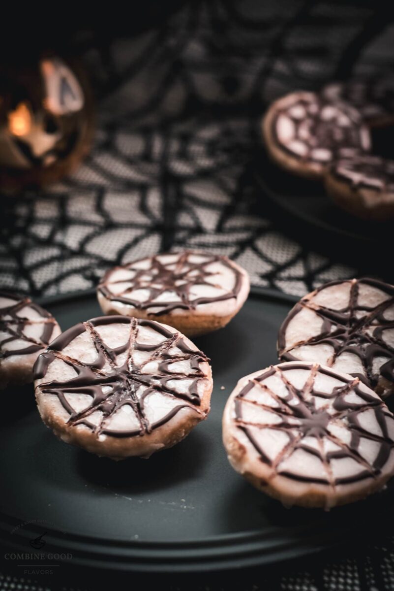 Hauntingly delicious spiderweb cookies, placed on black plate on spiderweb ground.