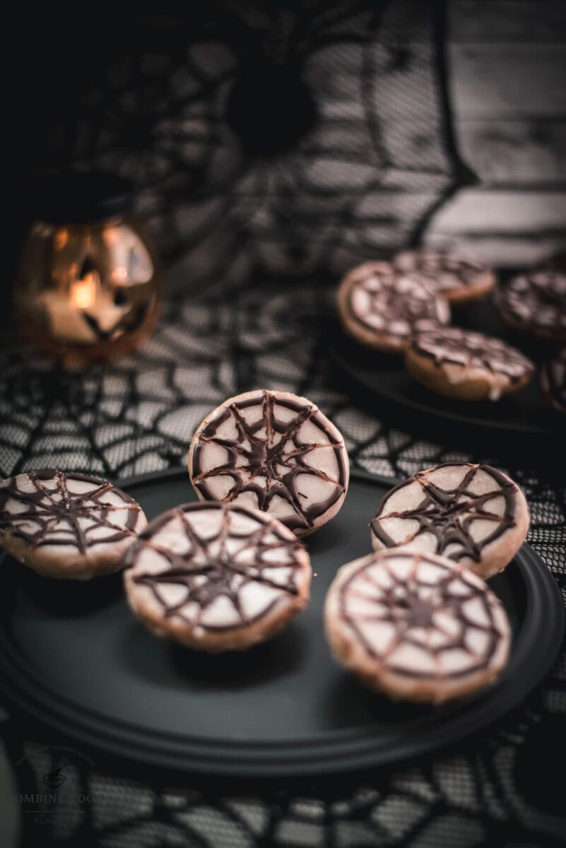 Hauntingly delicious spiderweb cookies, placed on black plate on spiderweb ground.