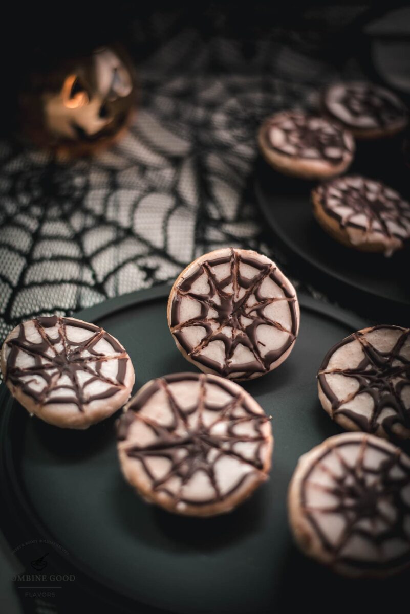 Hauntingly delicious spiderweb cookies, placed on black plate on spiderweb ground.