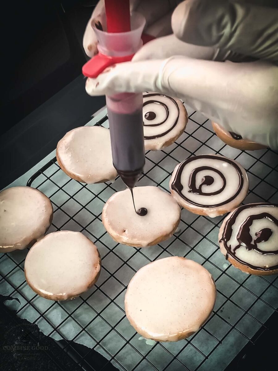 Drawing a chocolate dot in the middle of the cookie glaze, using a cake decorating pen.