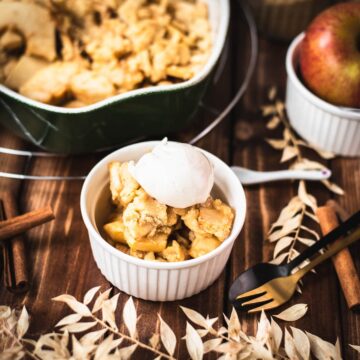 Serving bowl filled with freshly baked apple crisp topped with sour cream ice cream.