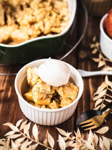 Serving bowl filled with freshly baked apple crisp topped with sour cream ice cream.