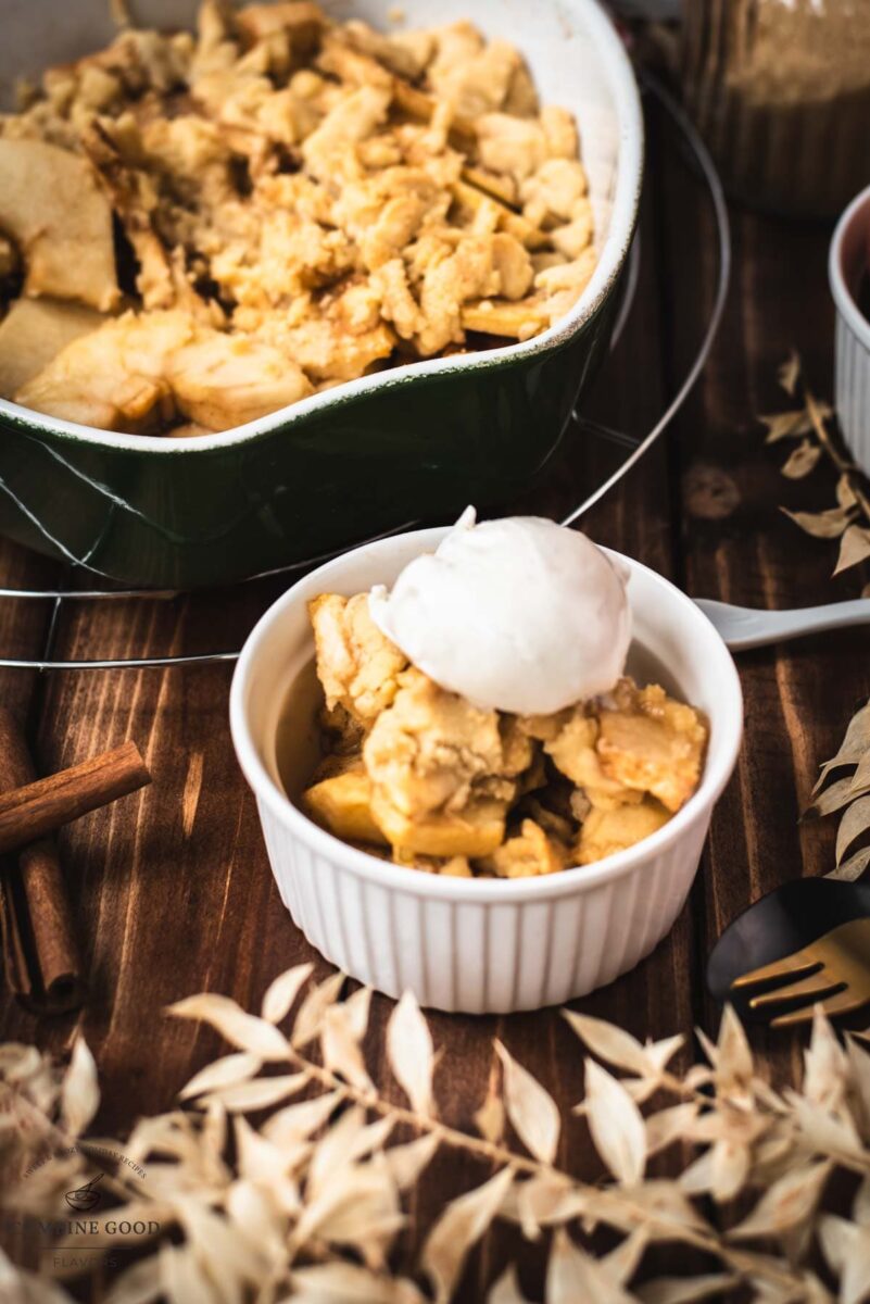 Serving bowl filled with freshly baked apple crisp topped with sour cream ice cream.