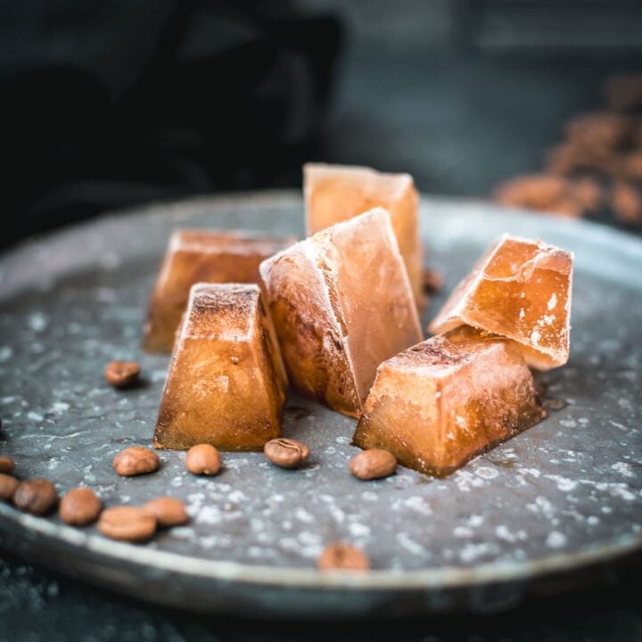 Frozen coffee cubes placed on metal plate next to coffee beans.