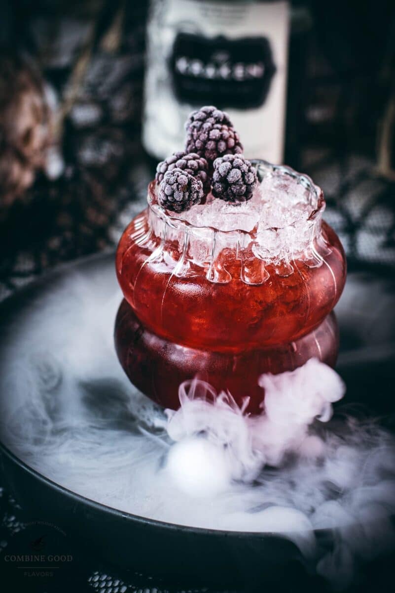 Spooky kramble cocktail, garnished with frozen blackberries and placed on a foggy plate.