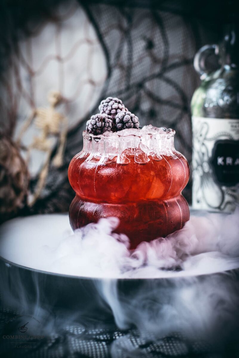 Spooky kramble cocktail, garnished with frozen blackberries and placed on a foggy plate.