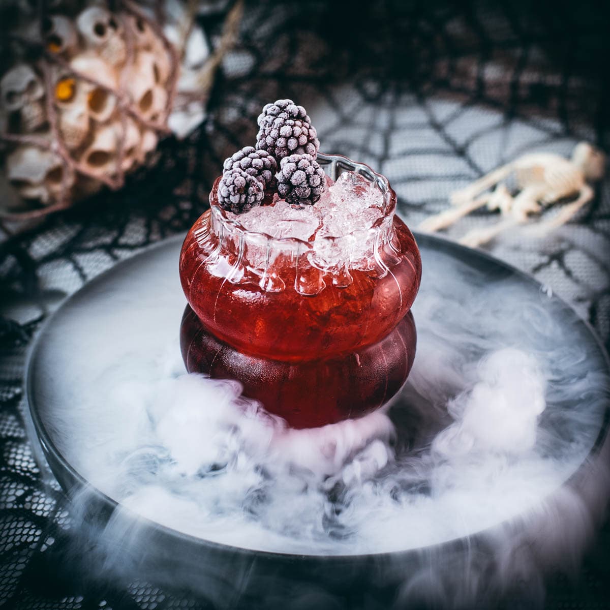 Spooky kramble cocktail, garnished with frozen blackberries and placed on a foggy plate.