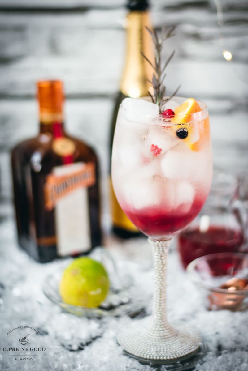 Gorgeous wineglass filled with delicious layered Prosecco cosmo. Garnished with a rosemary twig, an orange slice, and red and black currants.