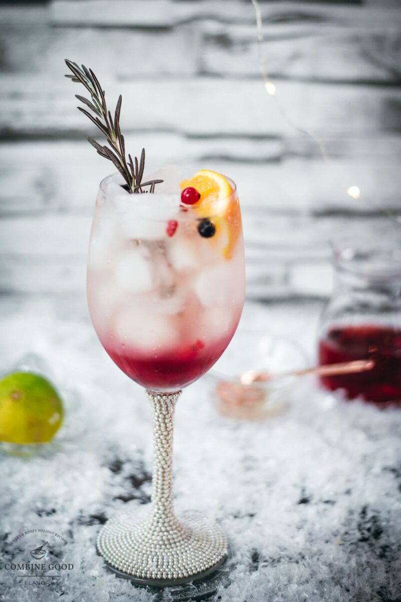 Gorgeous wineglass filled with delicious layered Prosecco cosmo. Garnished with a rosemary twig, an orange slice, and red and black currants.