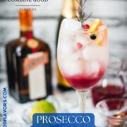 Gorgeous wineglass filled with delicious layered Prosecco cosmo. Garnished with a rosemary twig, an orange slice, and red and black currants.