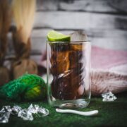 Twisted glass filled with a delicious Cuba Libre cocktail, placed on green felt mat.