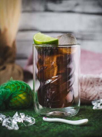 Twisted glass filled with a delicious Cuba Libre cocktail, placed on green felt mat.