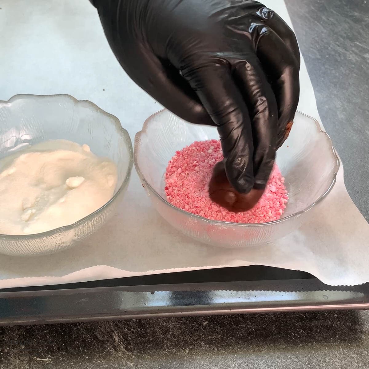 Hand with black gloves holding dough ball over a bowl filled with crushed candy canes.