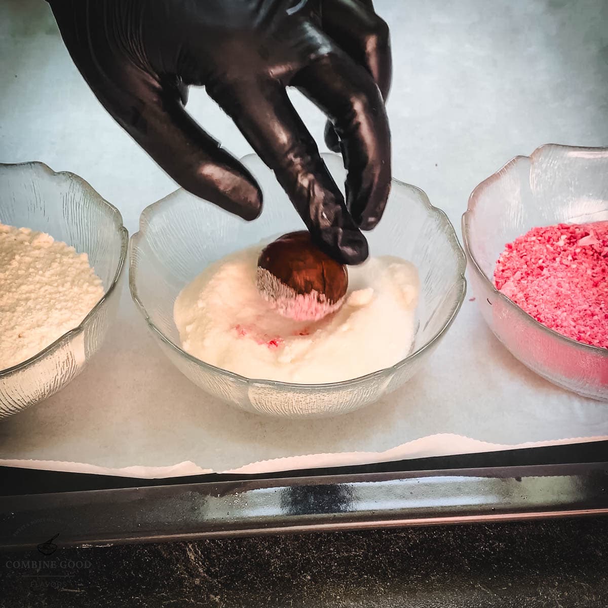 Hand with black gloves holding dough ball over a bowl filled with granulated sugar.