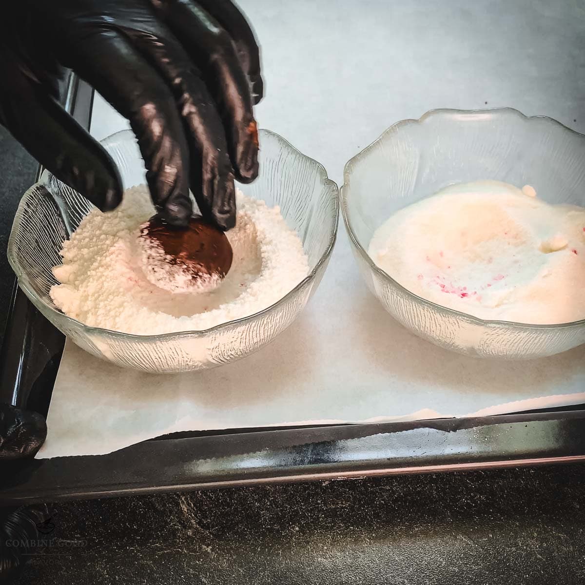 Hand with black gloves holding dough ball over a bowl filled with powdered sugar.