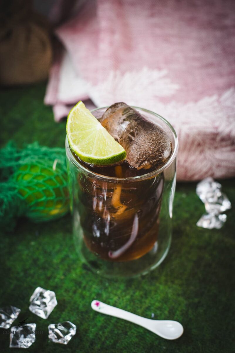 Twisted glass filled with a delicious Cuba Libre cocktail, placed on green felt mat.