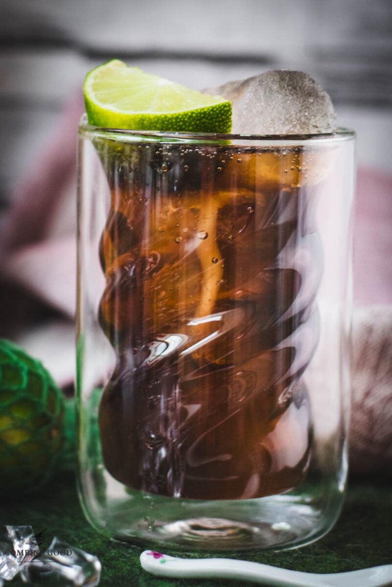 Twisted glass filled with a delicious Cuba Libre cocktail, placed on green felt mat.