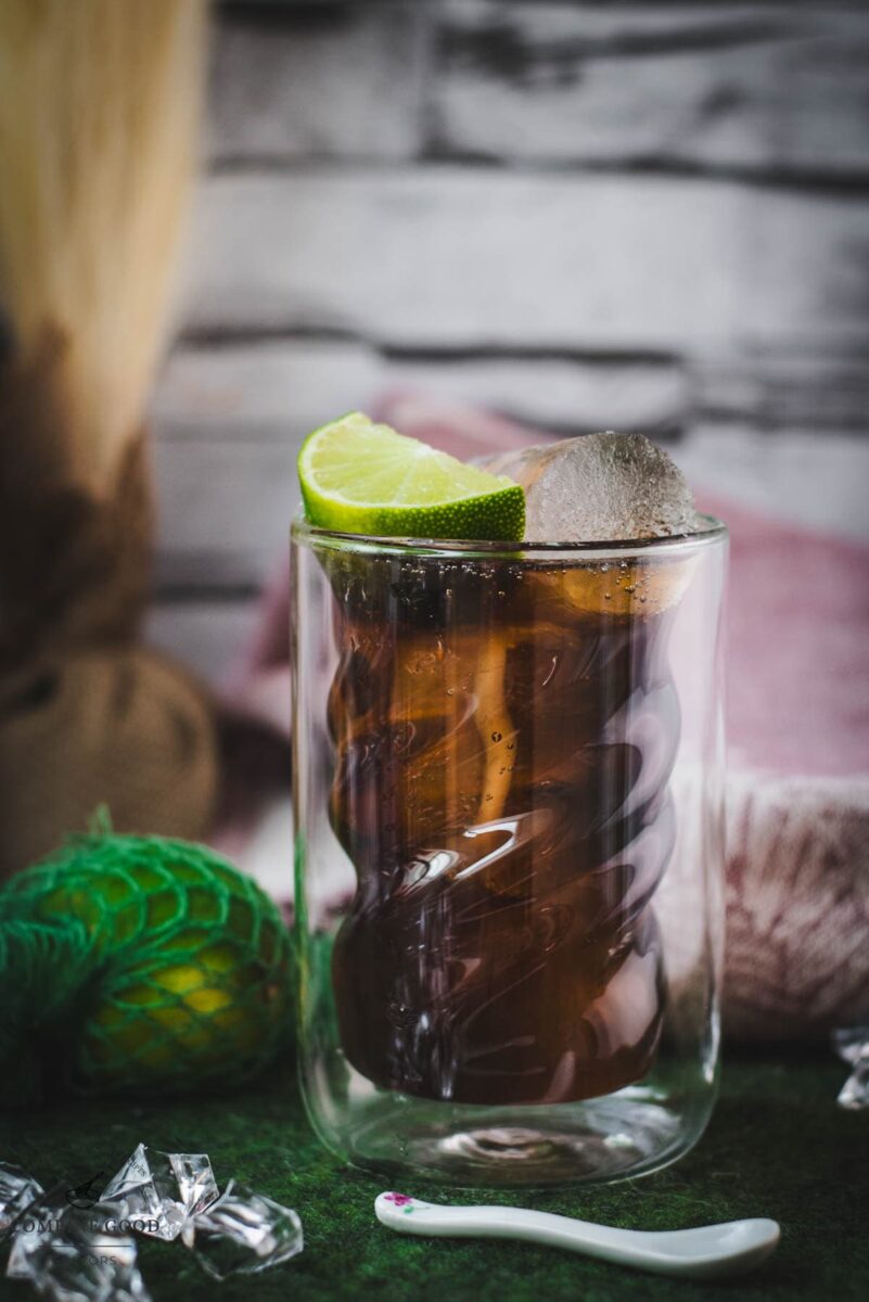 Twisted glass filled with a delicious Cuba Libre cocktail, placed on green felt mat.