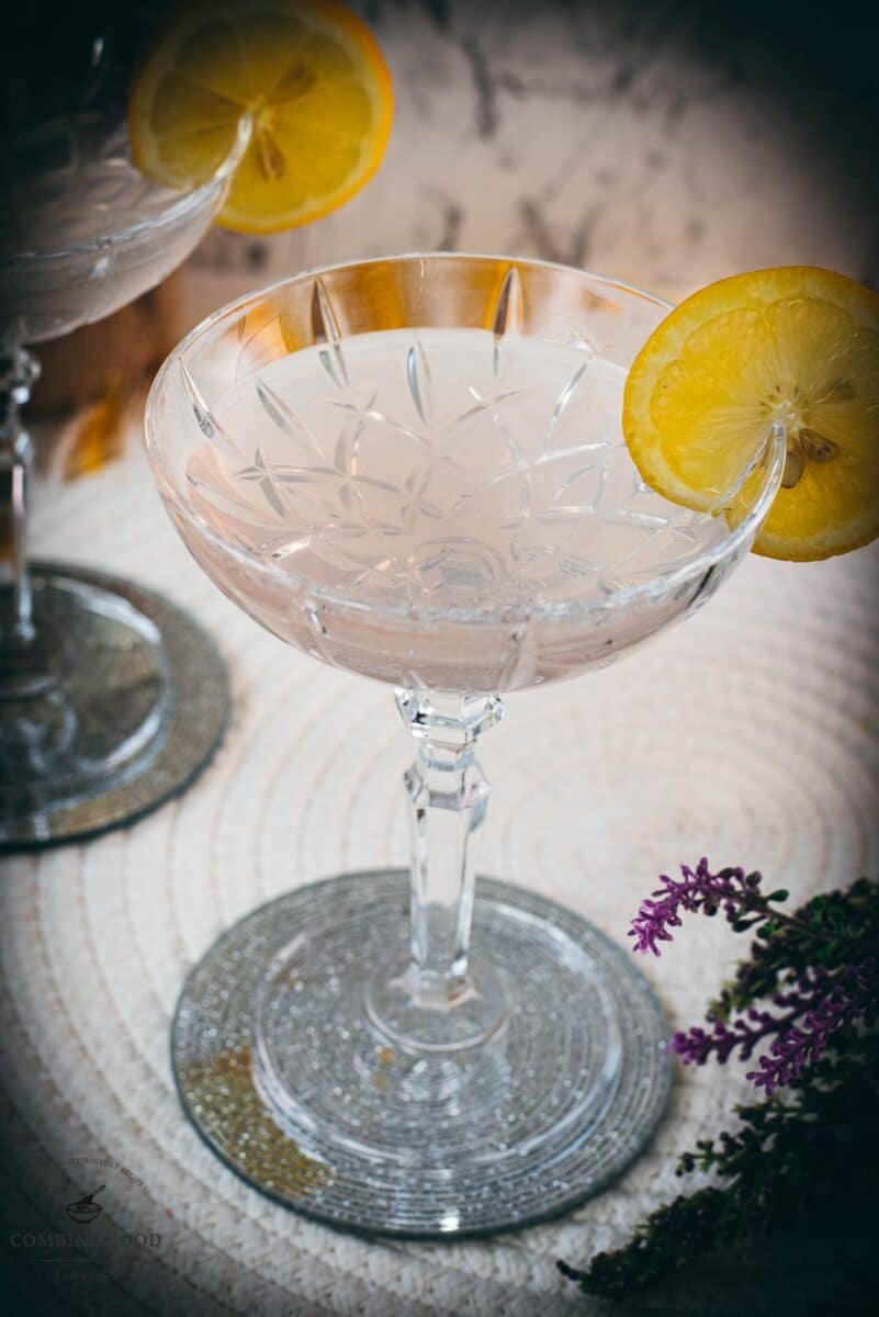 Elegant lavender gin spritz cocktail with prosecco, placed on a mirrored coaster, garnished with a lemon slice.