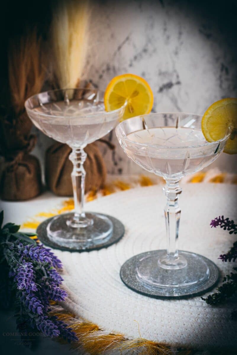 Elegant lavender gin spritz cocktail with prosecco, placed on a mirrored coaster, garnished with a lemon slice.