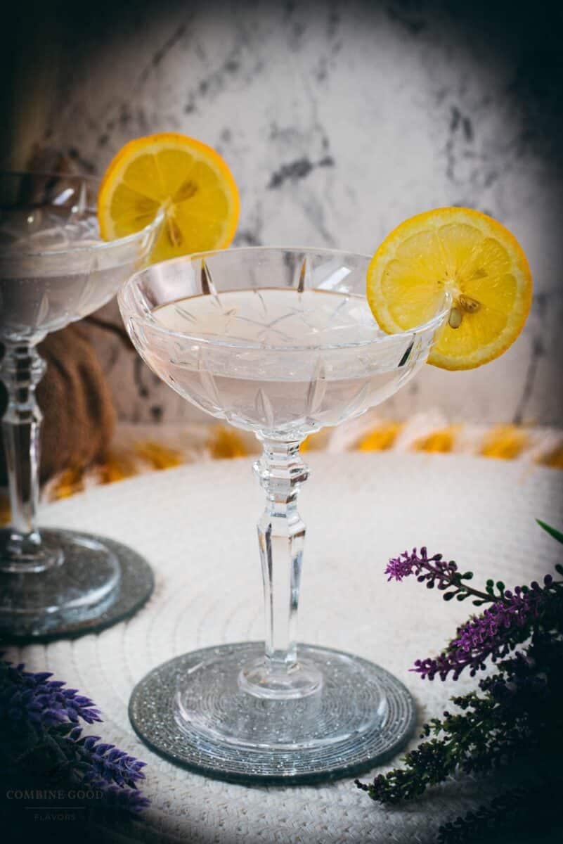 Elegant lavender gin spritz cocktail with prosecco, placed on a mirrored coaster, garnished with a lemon slice.