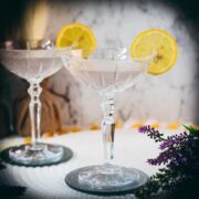 Elegant lavender gin spritz cocktail with prosecco, placed on a mirrored coaster, garnished with a lemon slice.