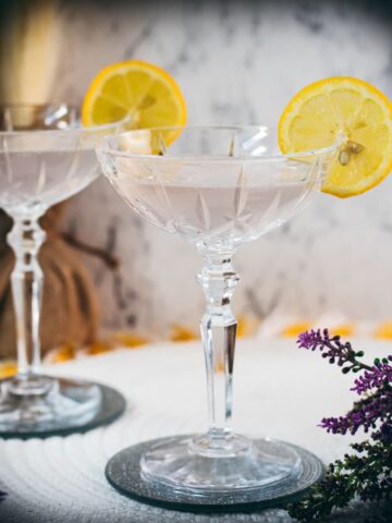 Elegant lavender gin spritz cocktail with prosecco, placed on a mirrored coaster, garnished with a lemon slice.