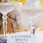 Elegant lavender gin spritz cocktail with prosecco, placed on a mirrored coaster, garnished with a lemon slice.