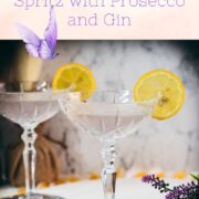 Elegant lavender gin spritz cocktail with prosecco, placed on a mirrored coaster, garnished with a lemon slice.