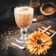 Rich French press Mexican coffee in gorgeous serving glass, placed on brown colored ground, next to orange-colored flower.