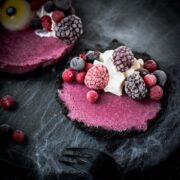 Hauntingly delicious mini Oreo tarts filled with a berry mix ganache, garnished with a creepy gummy eye, frozen berries and whipped cream. Placed on a black plate covered with spider webs.