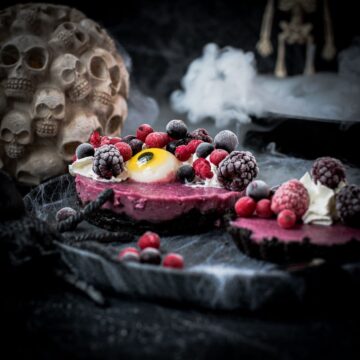 Hauntingly delicious mini Oreo tarts filled with a berry mix ganache, garnished with a creepy gummy eye, frozen berries and whipped cream. Placed on a black plate covered with spider webs.