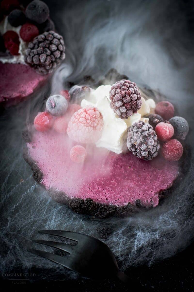 Hauntingly delicious mini Oreo tarts filled with a berry mix ganache, garnished with a creepy gummy eye, frozen berries and whipped cream. Placed on a black plate covered with spider webs.