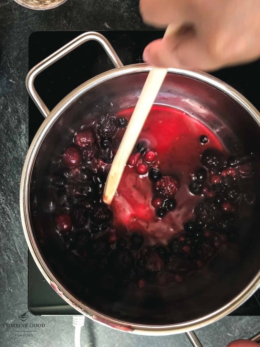 Stirring with a wooden spoon in a pan filled with a berry mix.