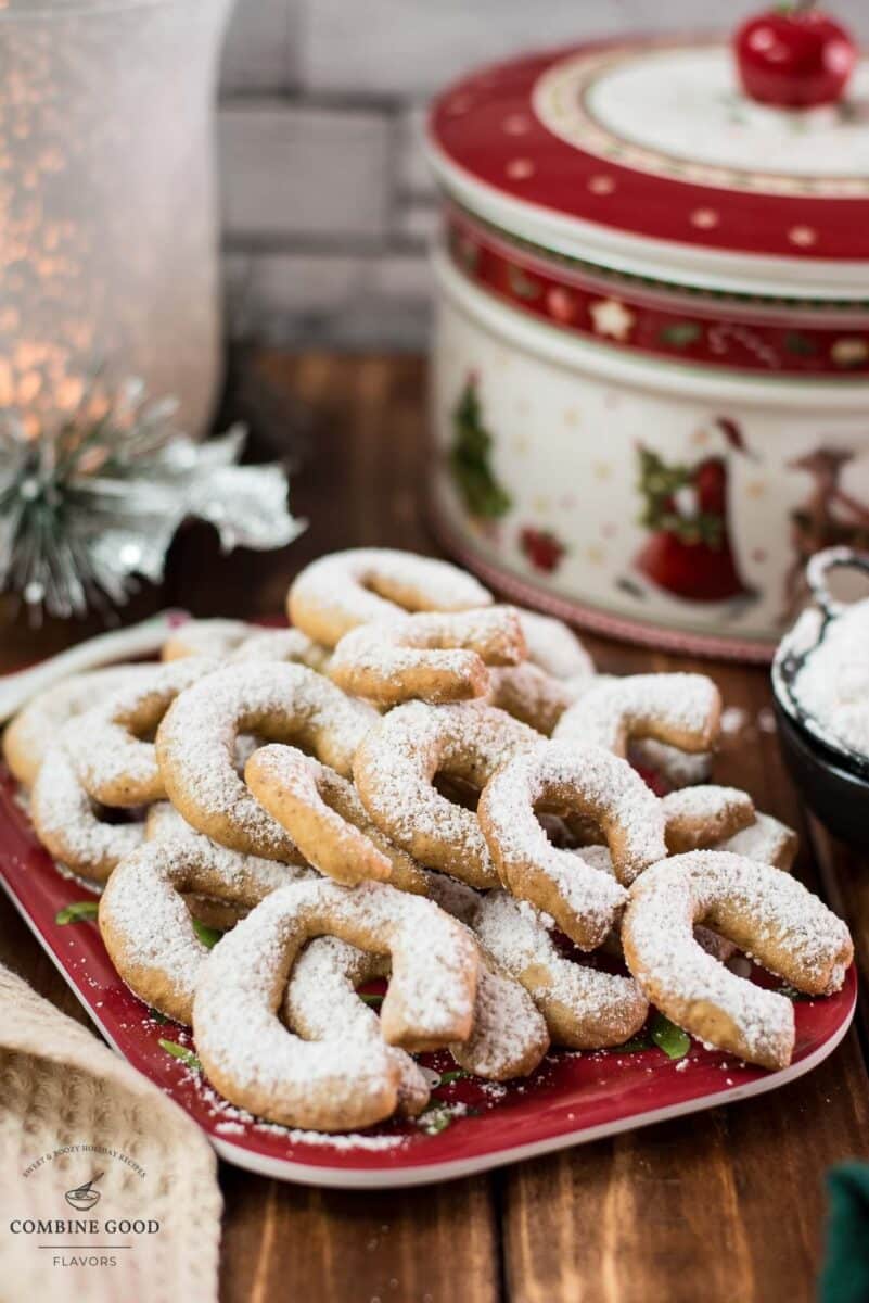 Delicious traditional Austrian vanilla crescents stacked on christmassy plate, placed next to a Christmass cookie jar.