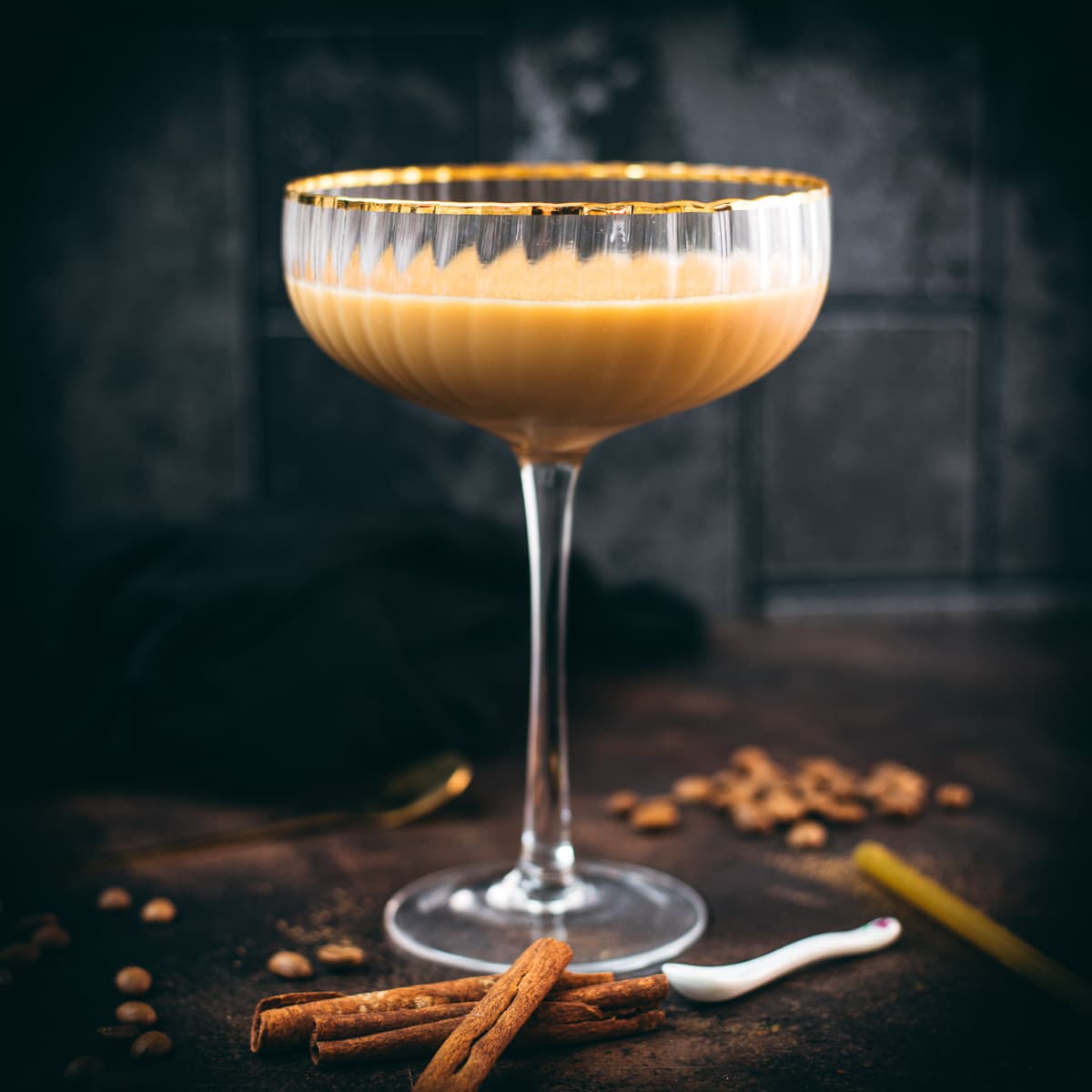 Gorgeous long stemmed cocktail glass with golden rim filled with a Cold Brew Kahlua Eggnog Cocktail, placed on dark ground.