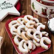 Delicious traditional Austrian vanilla crescents stacked on christmassy plate, placed next to a Christmass cookie jar.