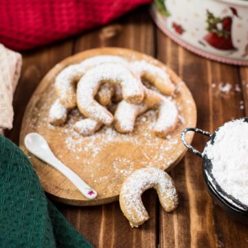 Delicious traditional Austrian vanilla crescents stacked on wooden plate, placed next to a Christmass cookie jar.