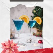 Gorgeous cocktail glasses filled with a stunning blue Christmas cocktail, garnished with an orange slice. Placed on mirrored coasters on snowy ground.